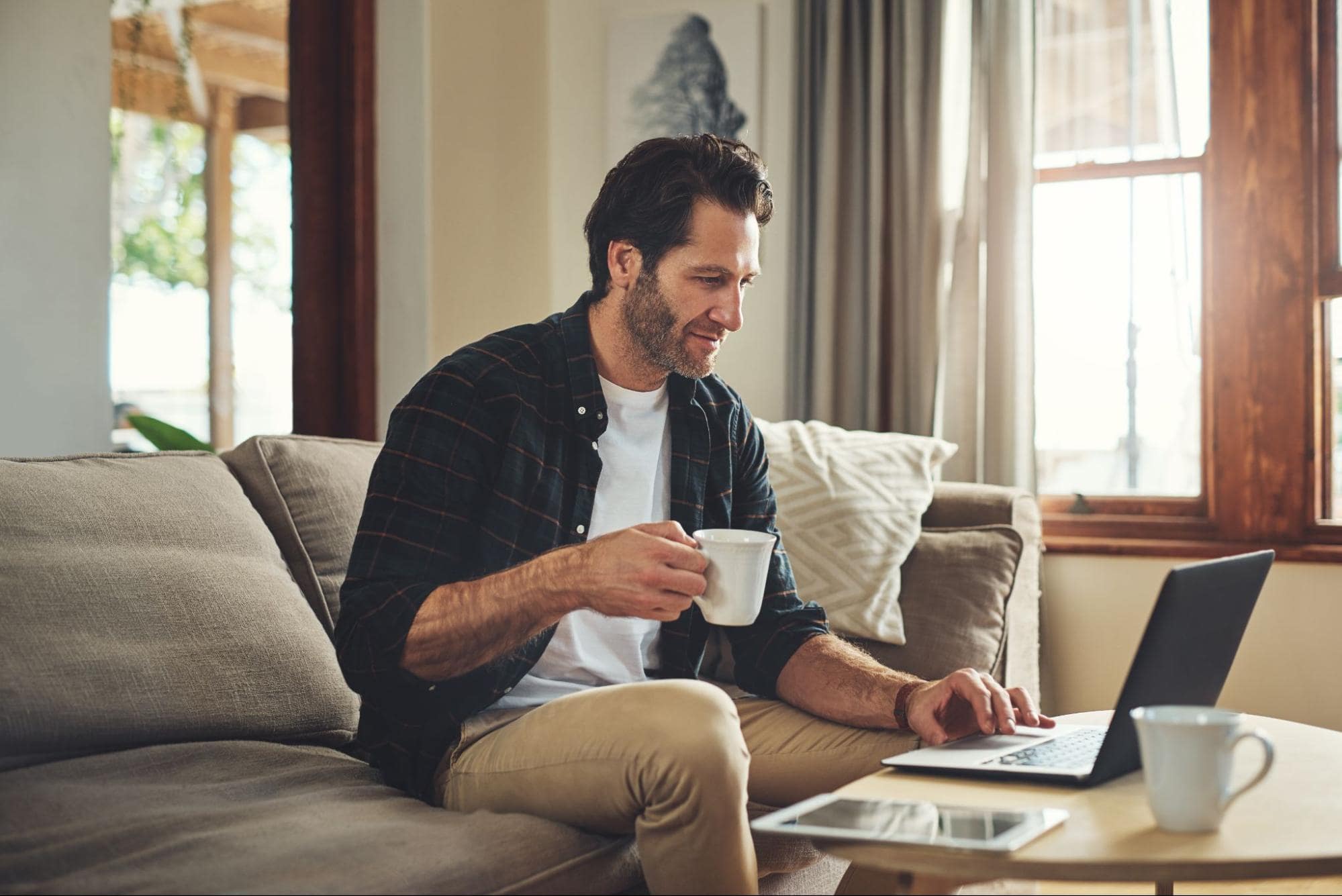 Young Man Drinking Coffee Reviewing Virtual Onboarding Tips on Laptop at Home