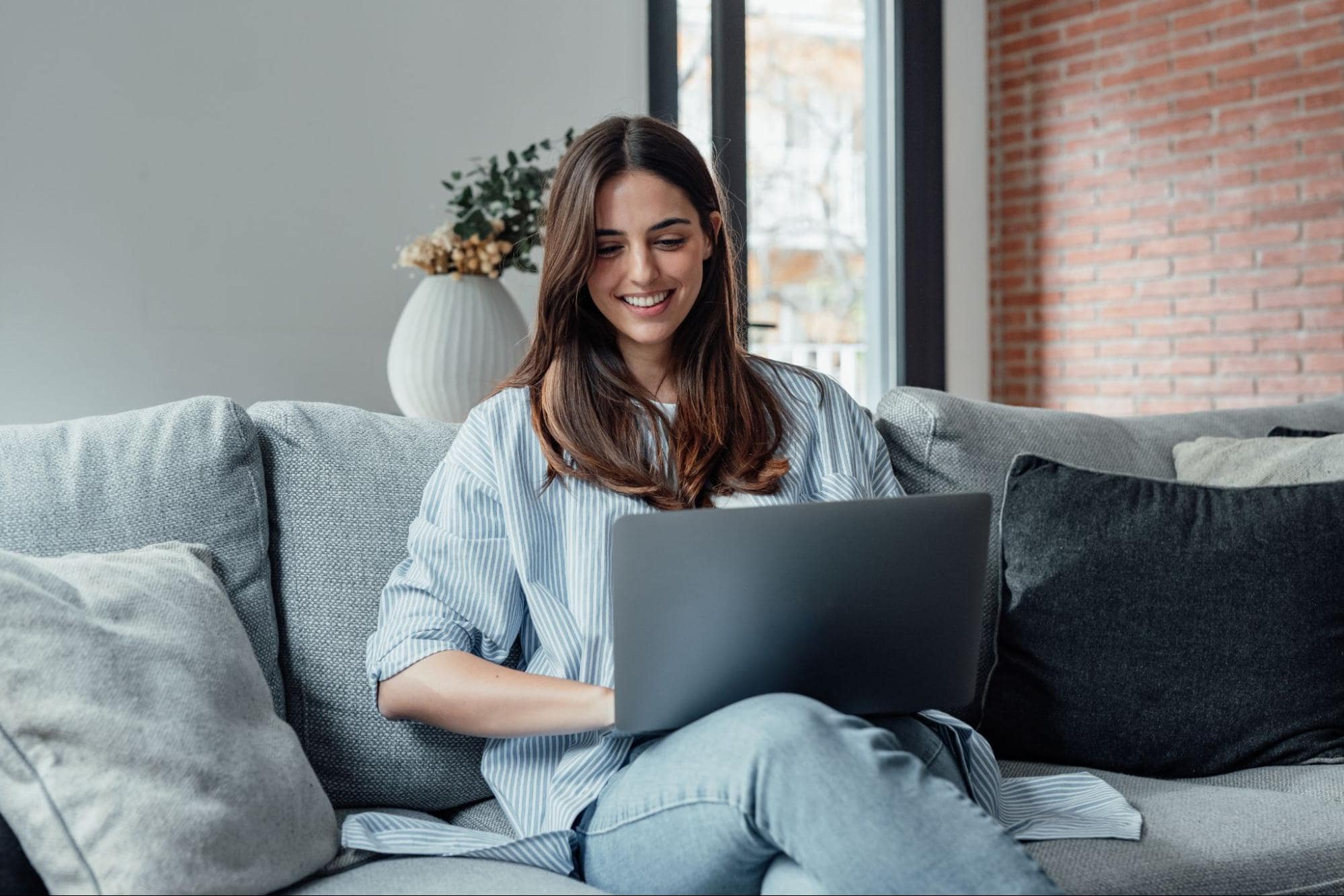 Smiling Young Woman Working on Laptop in Living Room at Home Participating in New Hire Onboarding