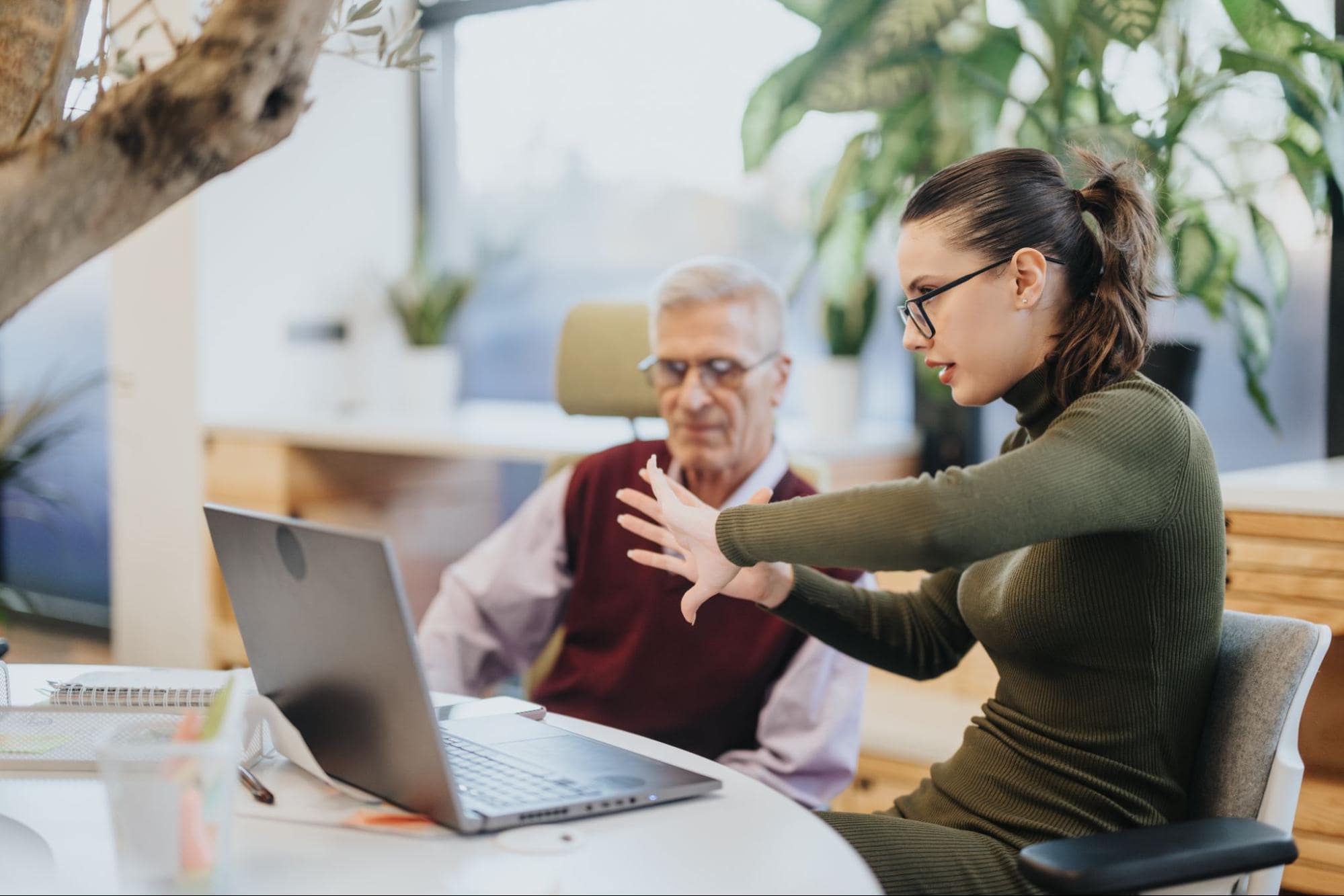 Young Woman and Retiree Discuss Silver Tsunami at Exit Interview in Front of Laptop in Modern Office