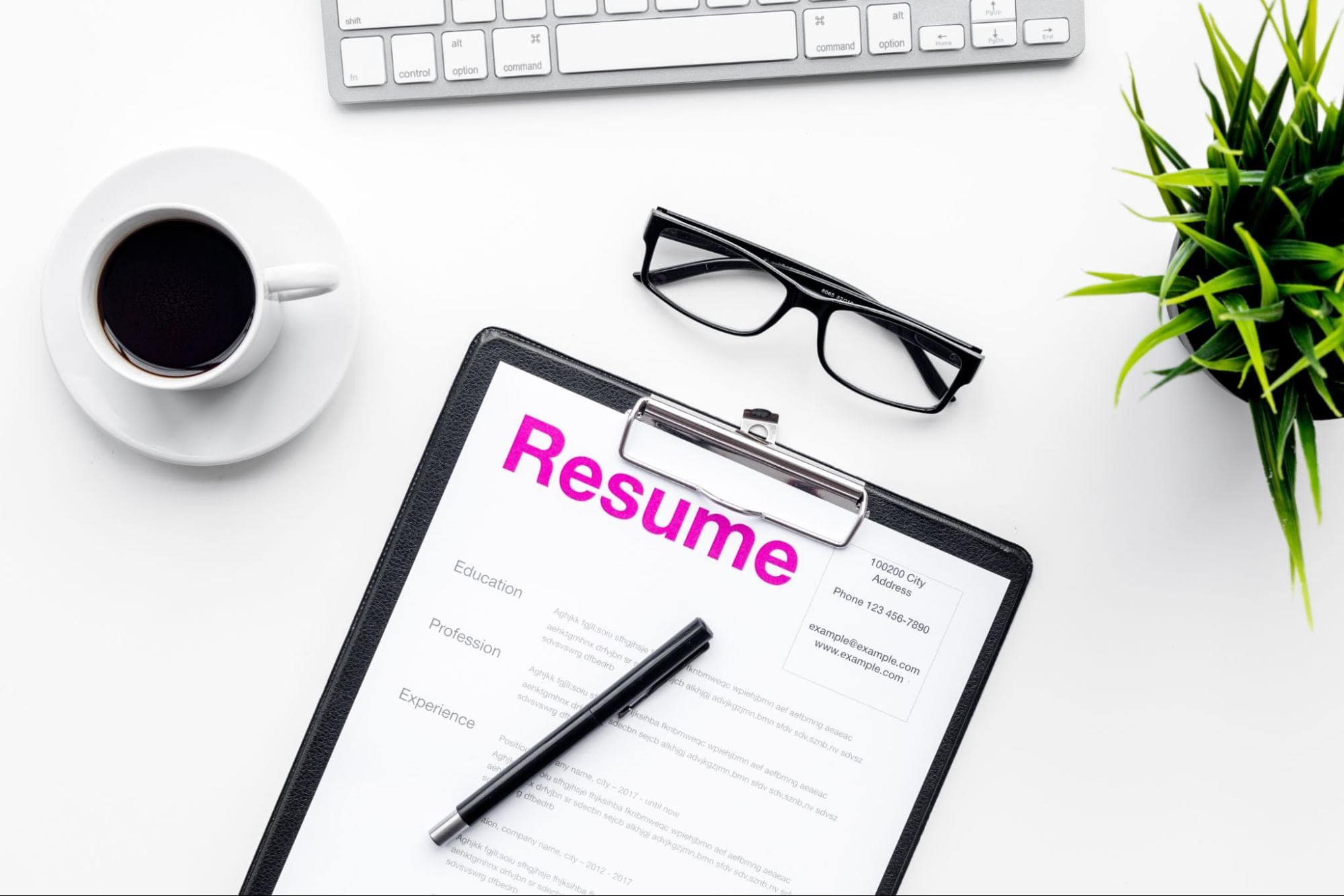 Closeup shot of an office desk with glasses, plant, coffee mug, keyboard and a manufacturing resume example
