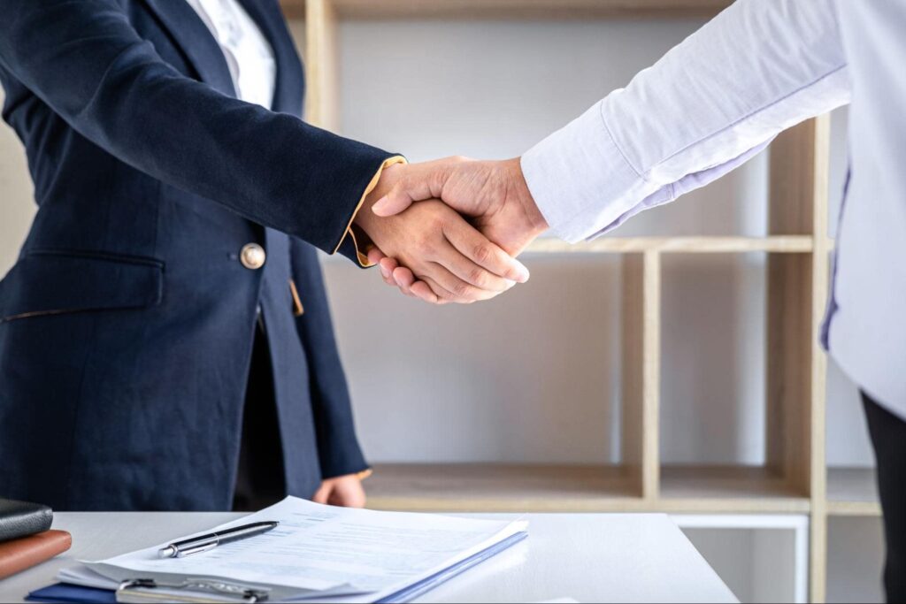 Two professionals shaking hands over a desk, representing a successful hire after learning how to write an underwriter job description.