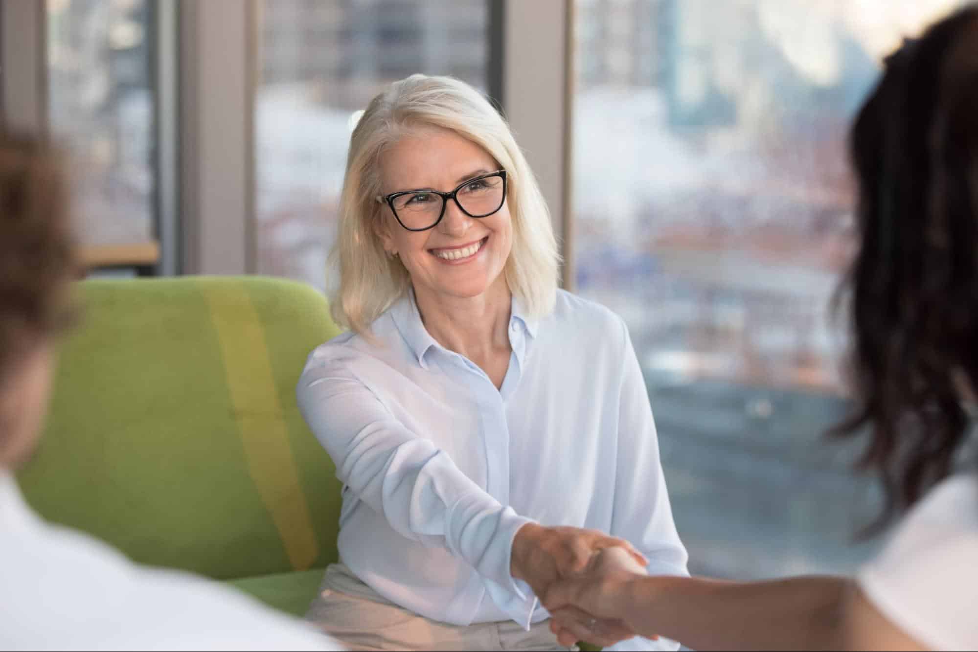 A smiling senior executive shaking hands with a colleague to ensure effective knowledge retention during a transition.