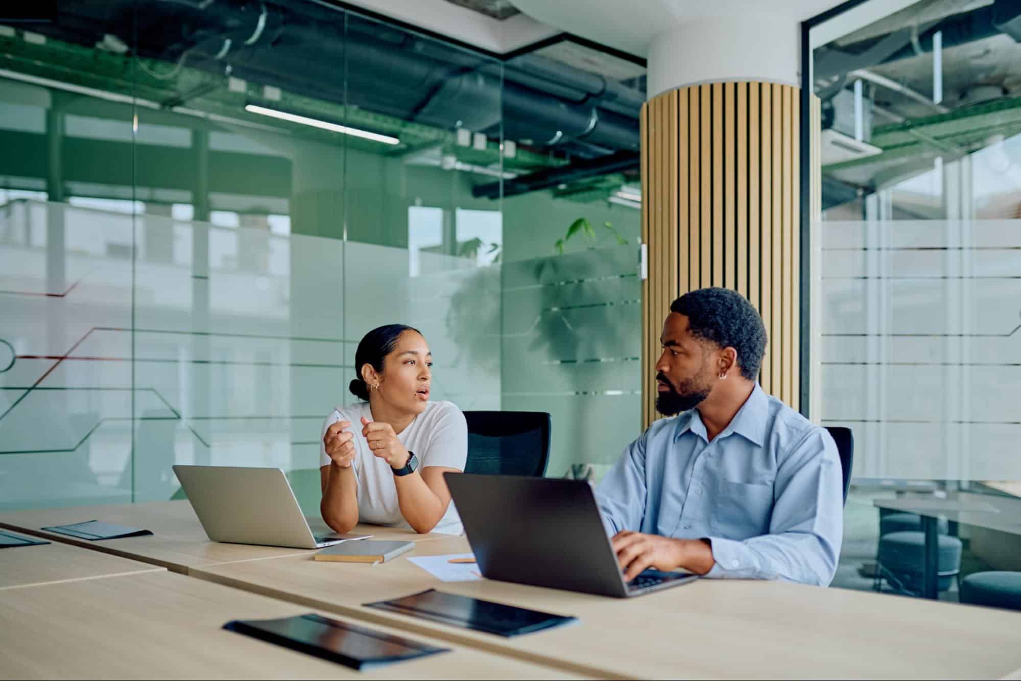 Two corporate staffing consultants discussing talent placement over laptops in a modern glass office, highlighting the collaborative process used by professional HVAC recruitment agencies.