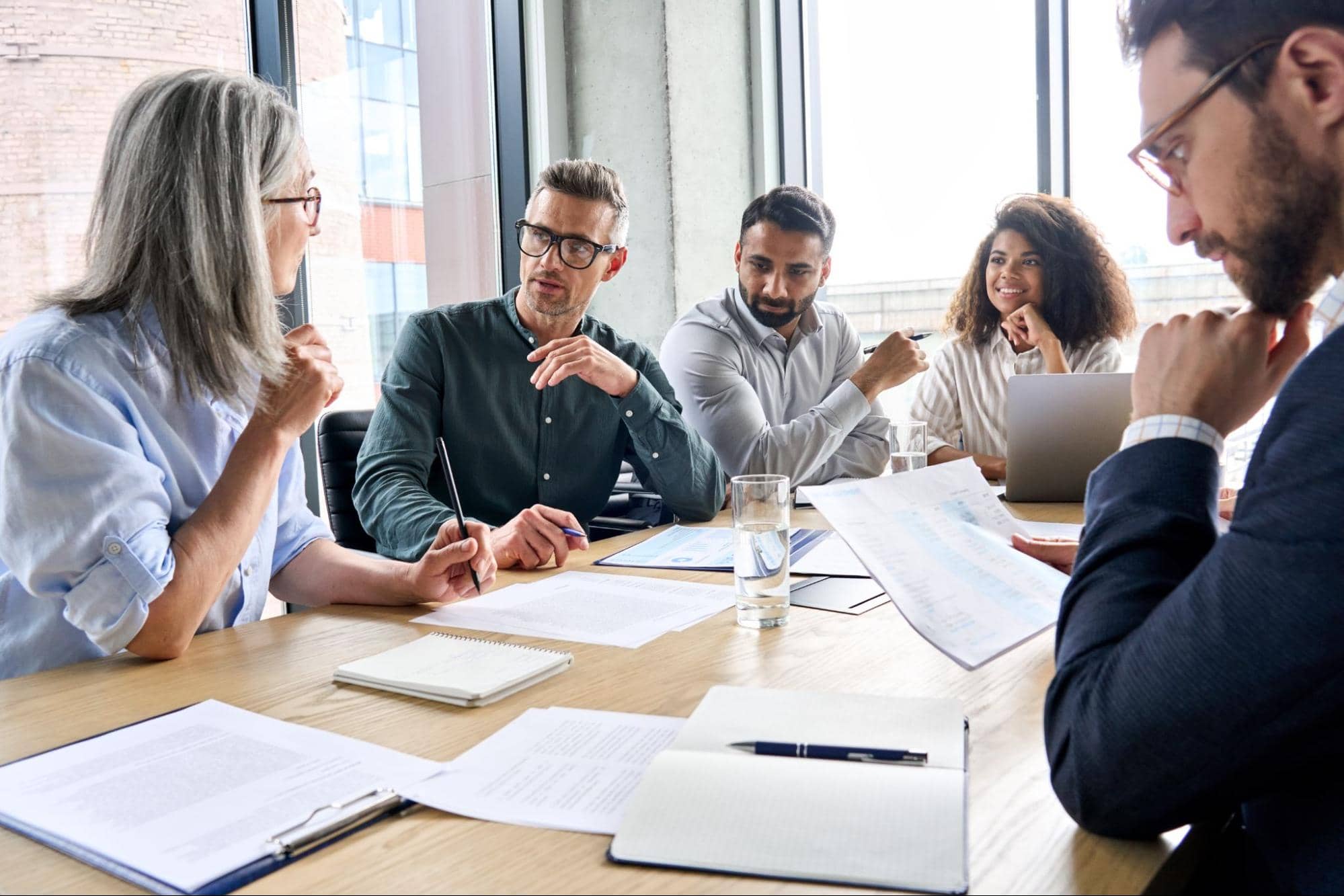 Diverse group of hiring professionals around a table reviewing documents during an executive search vs recruiting strategy meeting.