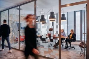Blurred professionals walk past a modern glass conference room where a team is collaborating on an insurance recruiting case study.