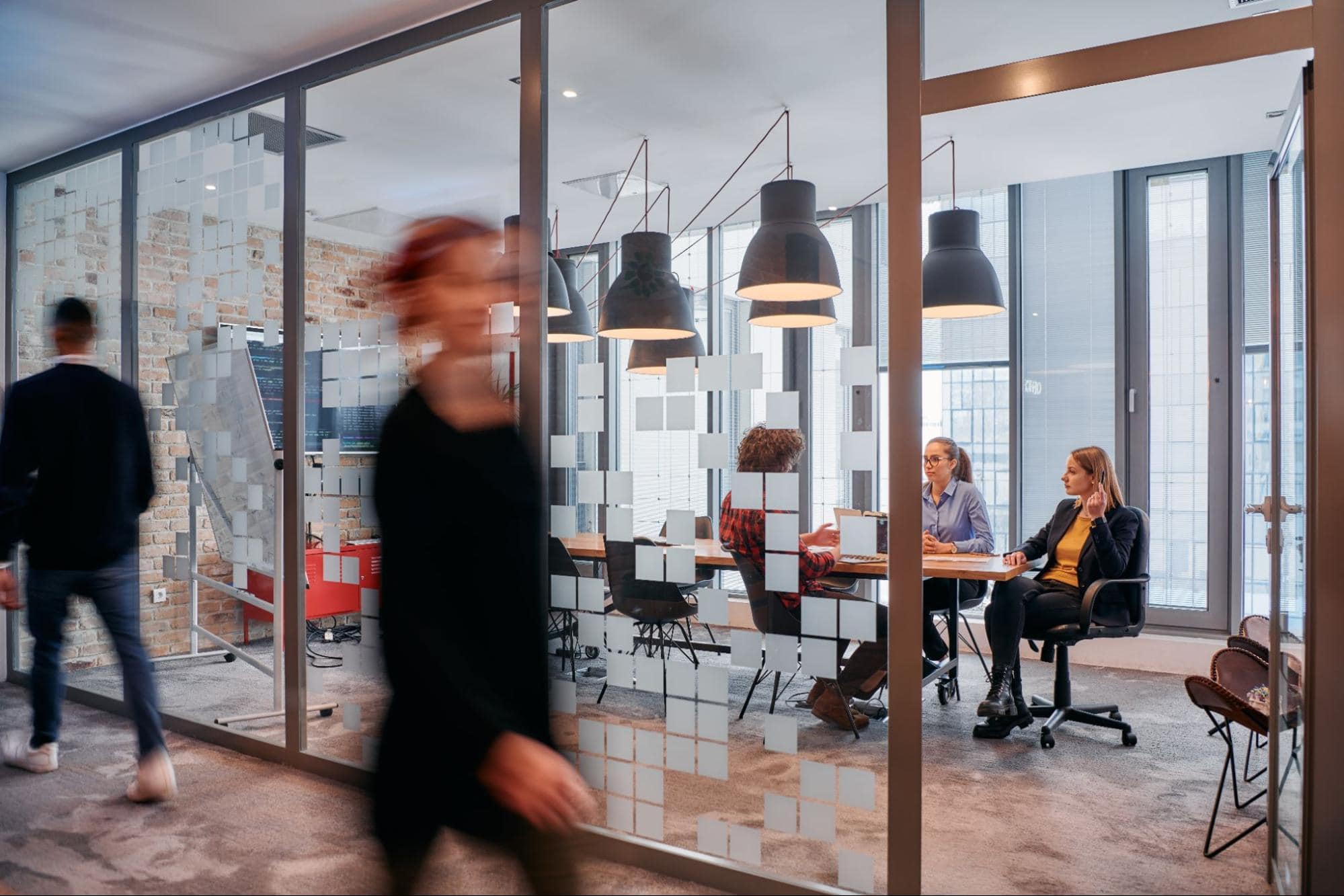 Blurred professionals walk past a modern glass conference room where a team is collaborating on an insurance recruiting case study.