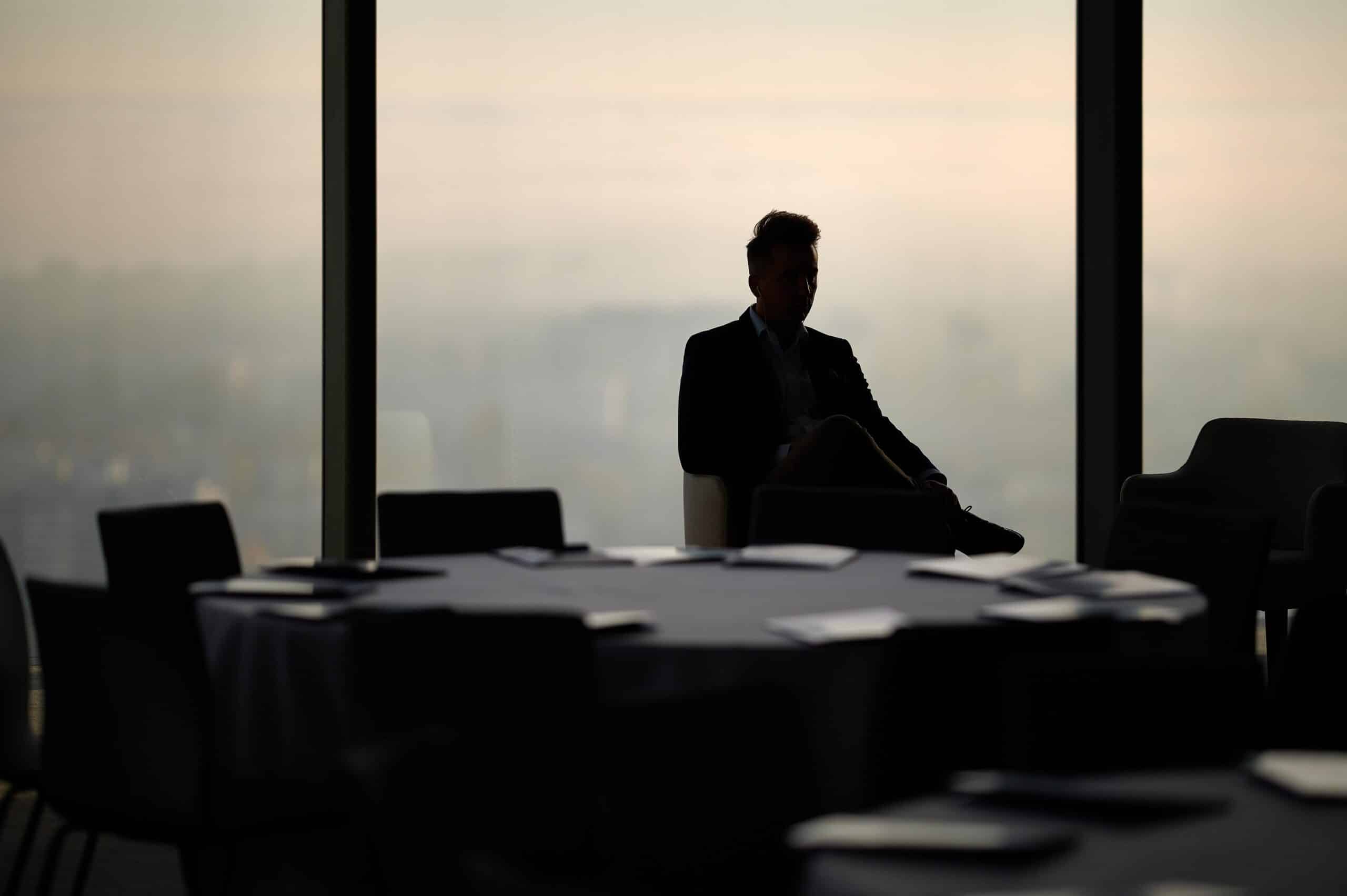Silhouette of an executive seated in an empty high-rise boardroom overlooking a city skyline during a confidential executive search