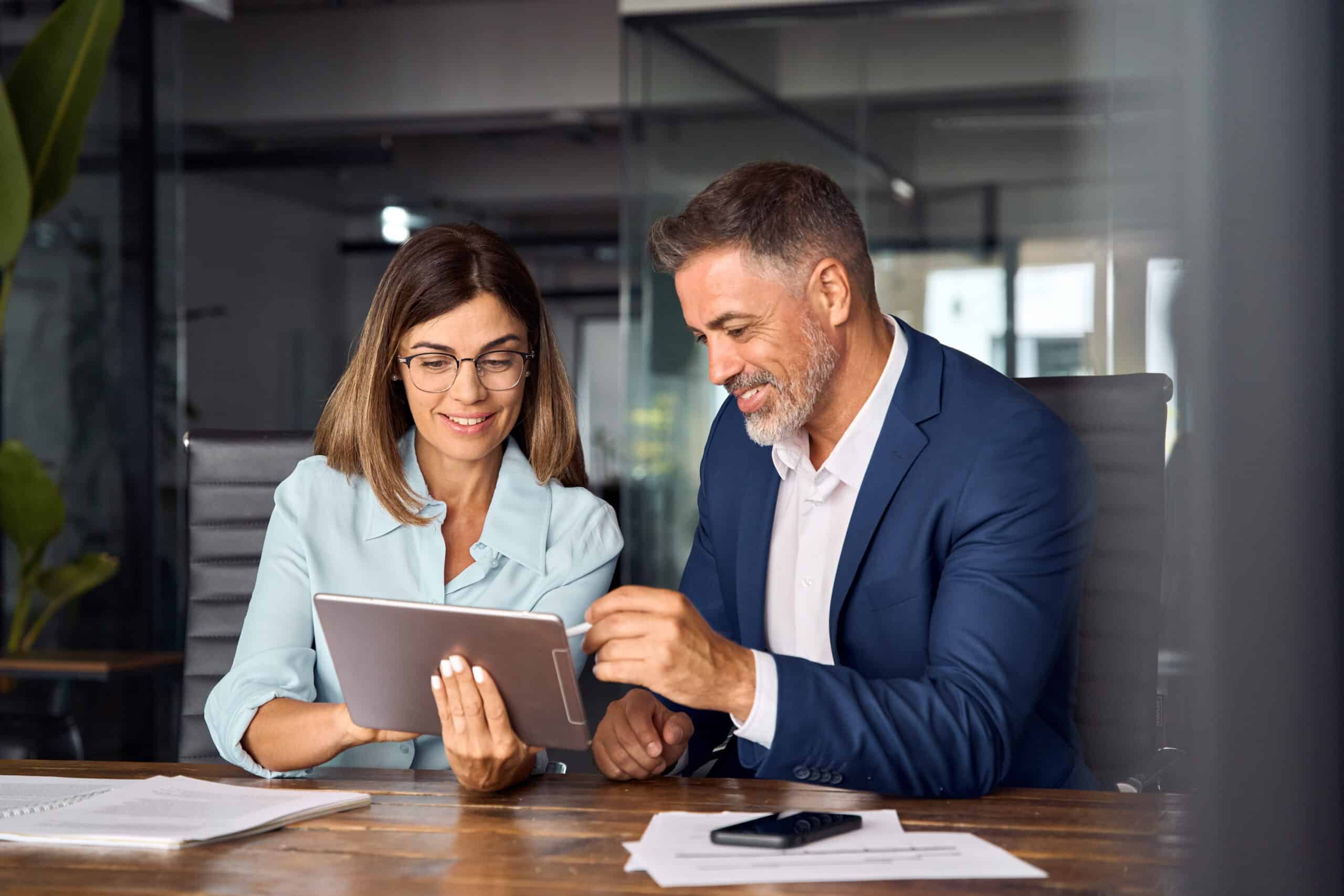 Real estate and property management recruiters reviewing candidate profiles on a digital tablet in a modern office.